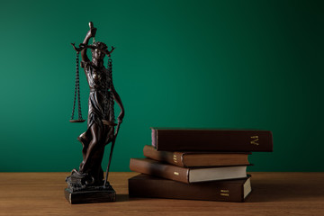 bronze statuette with scales of justice and volumes of books on wooden table on dark green background
