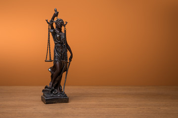 bronze statuette with scales of justice on wooden table on orange background