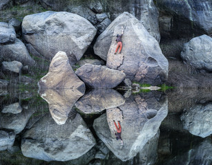 A man climbing on granite rocks reflected in the water of a river