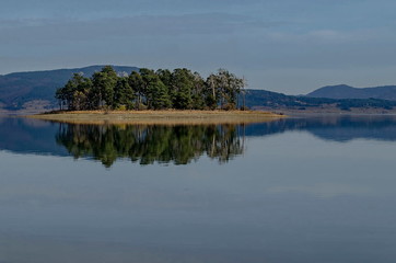 Panorama of Batak dam reservoir with island in the water and coastal autumn glade, forest, hill at Rhodope mountains, Bulgaria  