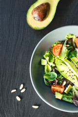 Healthy lunch with avocado. Green vegan lunch meal in bowl with green salad, spinach, arugula, avocado, tomatoes, seeds and pine nuts . Top view. Clean eating, dieting, vegan food concept