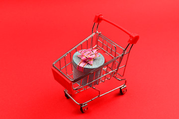 Blue present box with pink bow in a shopping cart on a red background.