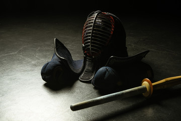 Kendo gloves, helmet and bamboo sword on dark surface