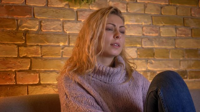Closeup shoot of adult caucasian blonde female watching TV being touched and melancholic while sitting on the couh indoors