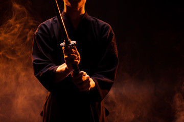Cropped view of young man in kimono holding kendo sword in smoke