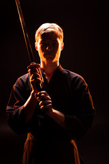 Young man in kimono holding kendo sword on black