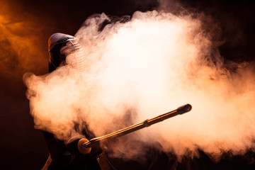 Kendo fighter in helmet holding bamboo sword in smoke