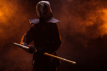 Kendo fighter in armor holding bamboo sword in smoke