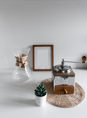 composition of hand coffee grinder in stainless material with drip pot glass in wood collar and wooden frame in the background / space for advertising / object isolated / interior design decoration