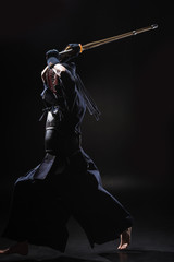 Full length view of kendo fighter in armor practicing with bamboo sword on black