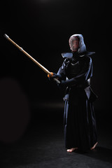 Full length view of kendo fighter in armor practicing with bamboo sword on black