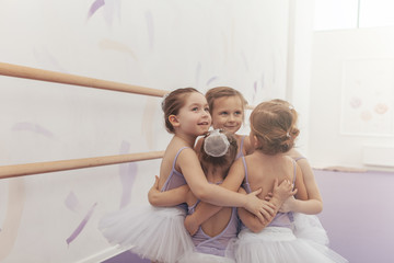 Adorable little girls in leotards and tutu skirts embracing, looking away joyfully. Group of cute...
