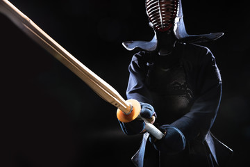 Kendo fighter in helmet holding bamboo sword on black