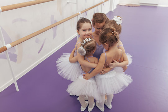 Top view shot of a group of cute little ballrinas wearing violet leotards and tutus hugging together after ballet class. Happy little girls embracing together at ballet school, copy space