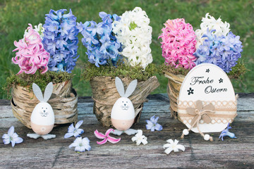 Frohe Ostern mit Hyazinthen und lustigen Ostereiern auf Holz