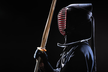 Side view of kendo fighter in traditional helmet holding bamboo sword on black