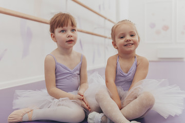Cute happy little girl wearing leotard and tutu skirs smiling to the camera sitting with her friend...