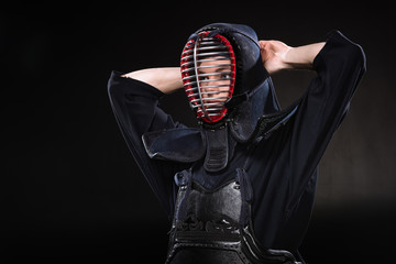 Kendo fighter in armor tying helmet and looking away on black
