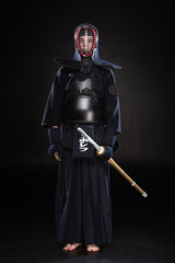 Full length view of kendo fighter in armor holding bamboo sword on black