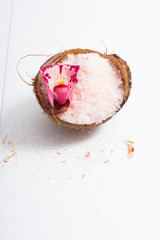 pile of pink bath salt with orchid flower at coconut shell bowl, white wood table