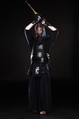 Full length view of kendo fighter in armor practicing with bamboo sword on black