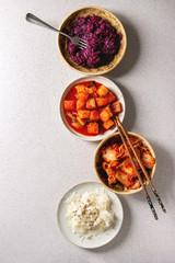 Fototapeta premium Variety of fermented food korean traditional kimchi cabbage and radish salad, white and red sauerkraut in ceramic plates with chopsticks and fork over grey spotted background. Flat lay, space