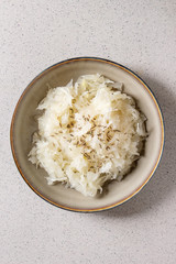 White sauerkraut chopped cabbage pickled in brine with cumin in ceramic plate over grey spotted background. Flat lay, space
