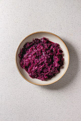 Obraz na płótnie Canvas Red sauerkraut chopped cabbage pickled in brine with cumin in ceramic plate over grey spotted background. Flat lay, space