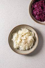 Red and white sauerkraut chopped cabbage pickled in brine with cumin in ceramic plate over grey spotted background. Flat lay, space