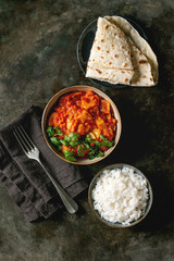 Vegan vegetarian curry with ripe yellow jackfruit served in ceramic bowl with rice, coriander and homemade flatbread flapjack over dark metal background. Flat lay, space