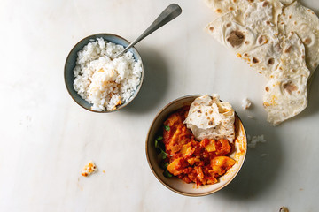 Started eaten Vegan vegetarian curry with ripe yellow jackfruit served in ceramic bowl with rice, coriander and homemade flatbread flapjack over white marble background. Flat lay, space