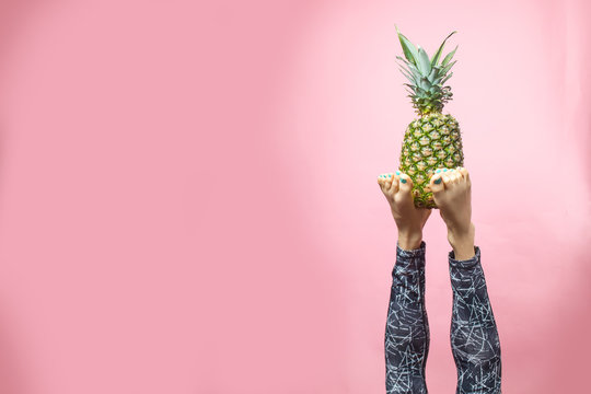 Sport and healthy eating lifestyle. Young woman doing yoga headstand and holding pineapple with her feet