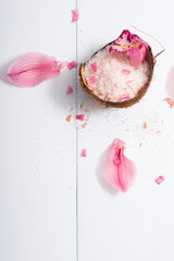 pile of pink bath salt with orchid flower petals at coconut shell bowl, white wood table