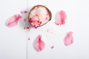 pile of pink bath salt with orchid flower petals at coconut shell bowl, white wood table