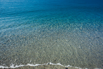 Background of transparent water of Mediterranean sea on a pebble beach