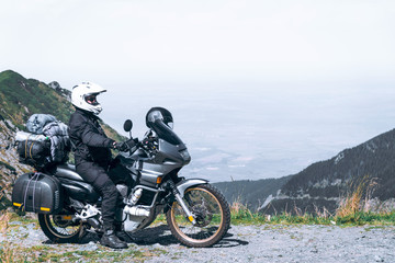 Obraz premium Biker is sitting on his adventure motorcycle, the top mountain in background, enduro, off road, beautiful view, danger road in mountains, freedom, extreme vacation. Transfagarasan Romania