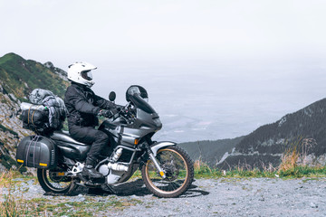 Biker is sitting on his adventure motorcycle, the top mountain in background, enduro, off road, beautiful view, danger road in mountains, freedom, extreme vacation. Transfagarasan Romania