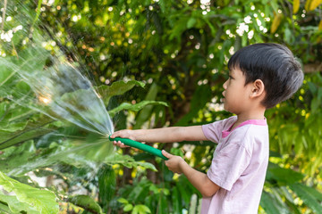 Children are watering plants with rubber hose in the garden.