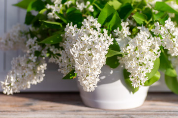 A bouquet of white lilac stands in a white vase on a wooden background. Fragrant spring bouquet.