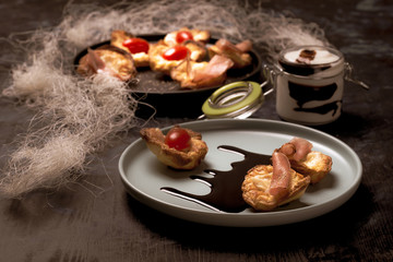 Few puff pastry cups filled by cheese and ham on blue plate with dark sauce