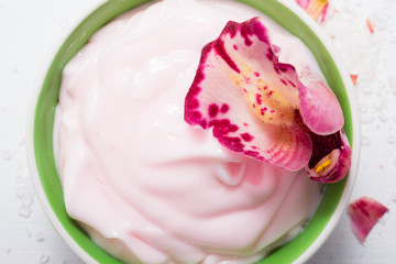 cosmetic cream with pink flower petals, white wood table