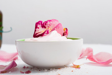 cosmetic cream with pink flower petals, white wood table