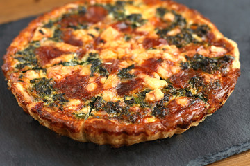 Italian traditional rustic quiche pizza with cheese, spinach  and tomatoes on a black plate in restaurant