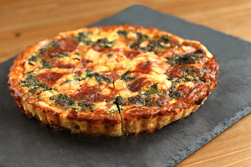 Italian traditional rustic quiche pizza with cheese, spinach  and tomatoes on a black plate in restaurant