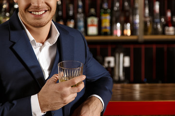 Passionate for high quality. Cropped shot of a handsome elegant man in a suit smiling enjoying his whiskey at the bar copyspace on the side 