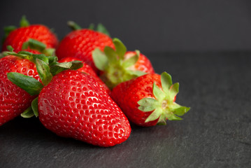 Close-up of strawberries with green leaves on slate stone