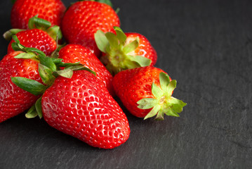 Close-up of strawberries with green leaves on slate stone with copy space