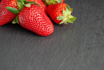 Top view of strawberries with green leaves on slate stone