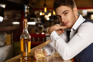 Mind if I join? Shot of an attractive young man looking to the camera seductively sitting at the bar having a glass of whiskey 
