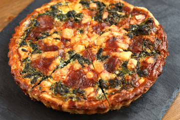 Italian traditional rustic quiche pizza with cheese, spinach  and tomatoes on a black plate in restaurant